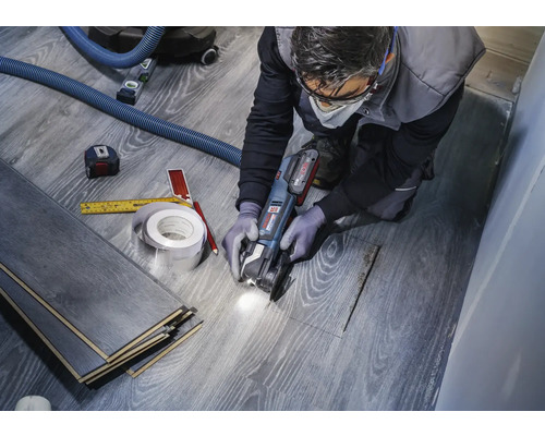 En hantverkare skär laminat med en multifunktionell verktygsmaskin för att skapa en utskärning för ett rör. Verktyg som ett måttband och en penna finns till hands.