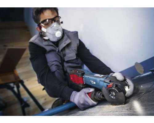 Man arbetar med en vinkelslip på ett golv, personlig skyddsutrustning finns