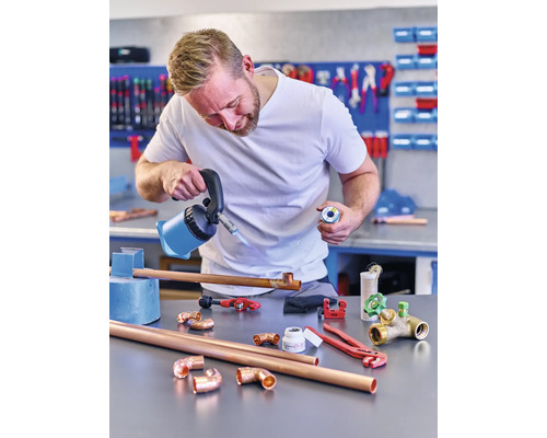 Man löder kopparrör med lödlampa och lödtenn i en verkstad.