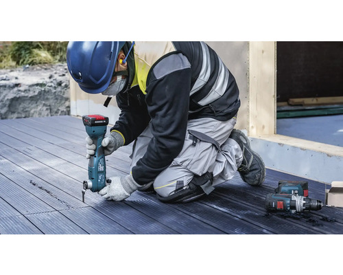 En arbetare använder ett multifunktionsverktyg på en träterrass. Personlig skyddsutrustning finns också.