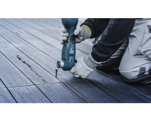 En person arbetar med ett multifunktionellt verktyg på en träterrass.