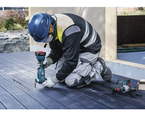 Hantverkare knäböjer på en terrass och arbetar med ett multifunktionsverktyg