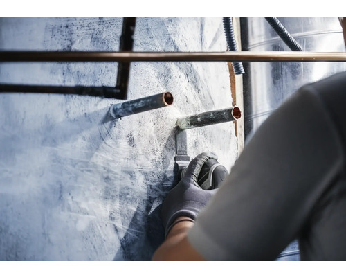 En rörmokare löder kopparrör på en vägg.