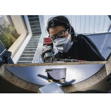 Kvinna med skyddsglasögon och dammmask arbetar med en multikvarn på ett arbetsstycke