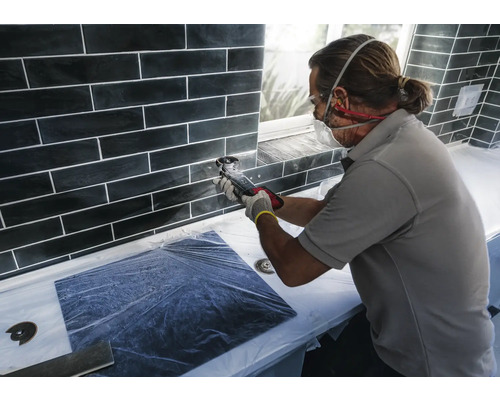 Kakelsättare som arbetar med ett multifunktionsverktyg på en vägg med svarta plattor.