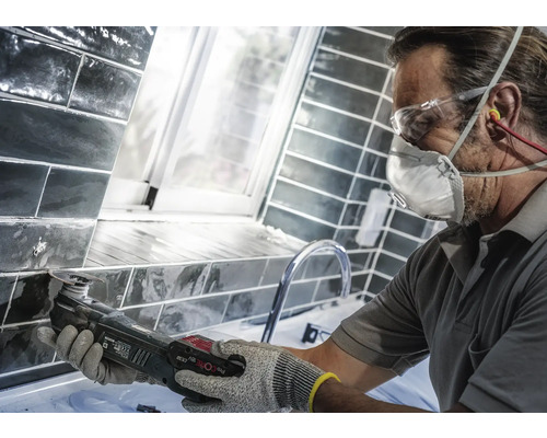 Hantverkare arbetar med ett multifunktionellt verktyg på kakel i ett badrum