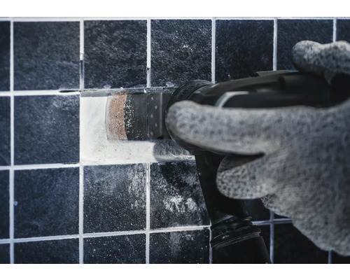 Hantverkare tar bort en kakelplatta med ett multifunktionsverktyg.