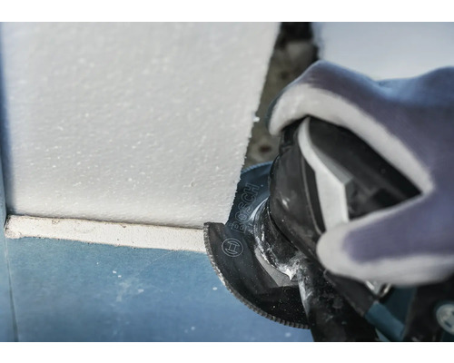 Hantverkare som arbetar med en oscillerande såg för att skära material på en byggarbetsplats. Bosch-logotyp.