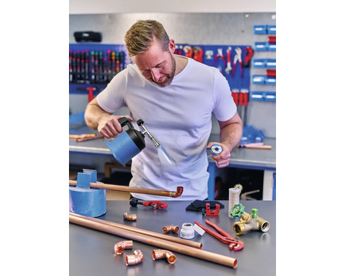 Man löder kopparrör med en brännare, lod och diverse verktyg på en arbetsbänk.