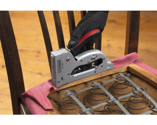 En hand med handske fäster tyg med en häftpistol på en stol.