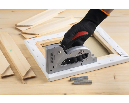 Hand med handske använder en häftpistol på en duk