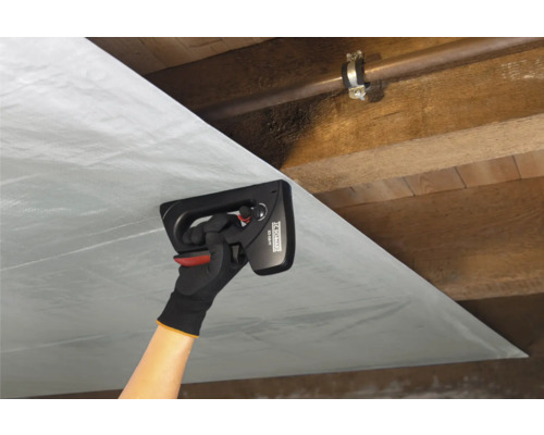 En person fäster ångspärrsfolie med en manuell häftpistol i ett trätak.