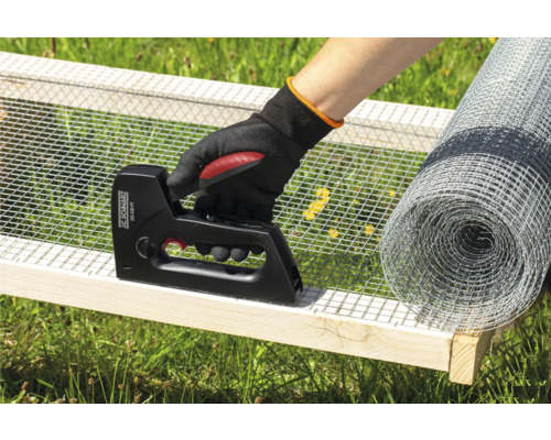 En person fäster metallnät med en häftpistol på en träram, med en rulle metallnät i bakgrunden.