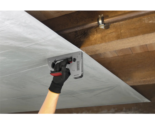 Person fäster ångspärrsfolie med en häftpistol i ett trätak.