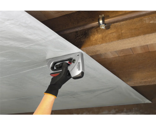 En person fäster folie med en handtacker på ett trätak.