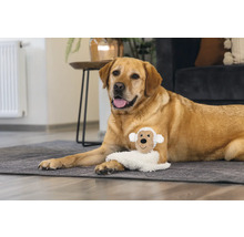 En labrador ligger med en fårplyschleksak på en matta.