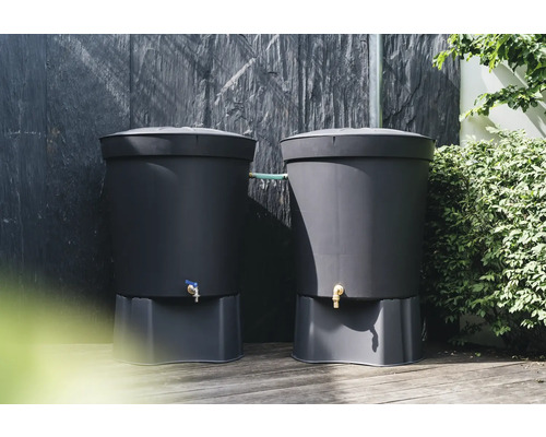 Två mörka regntunnor i plast med sockel och kran framför en mörk vägg