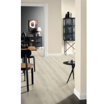 Interiör med ljust laminatgolv, stolar och dekorativa föremål på bord och i ett vitrinskåp.