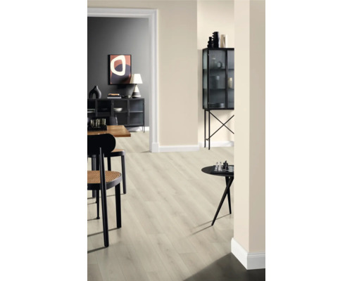 Interiör med ljust laminatgolv, stolar och dekorativa föremål på bord och i ett vitrinskåp.