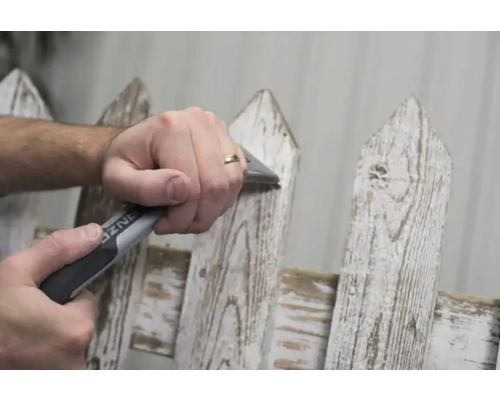 En person använder ett avgradningsverktyg på ett trädgårdsstaket.