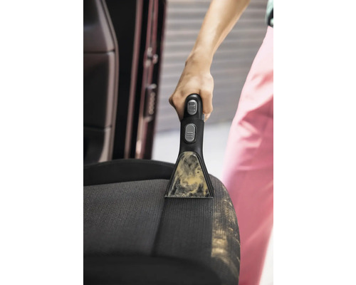 Närbild av en person som rengör en bilbarnstol med en bärbar fläckrengörare.