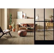 Vardagsrum med soffa, fåtölj, bord, golvlampa, byrå, dekoration och krukväxter på trägolv.