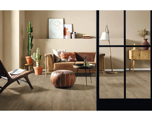 Vardagsrum med soffa, fåtölj, bord, golvlampa, byrå, dekoration och krukväxter på trägolv.