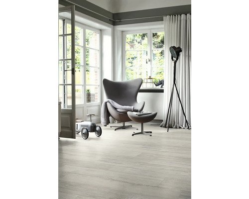 Ljust vardagsrum med fåtölj, läslampa och leksaksbil på trägolv