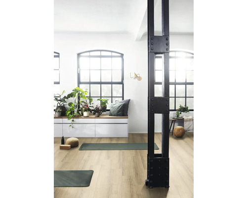 Ljust rum med stora fönster, växter, yogamattor och en svart metallpelare