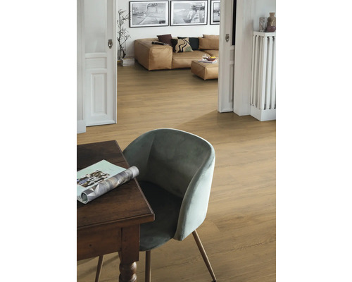 Interiörbild av ett rum med trägolv, ett bord, en stol och en vardagsrumsdel i bakgrunden.