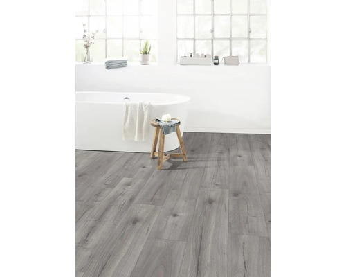 Ljust badrum med badkar, pall och grått laminatgolv.