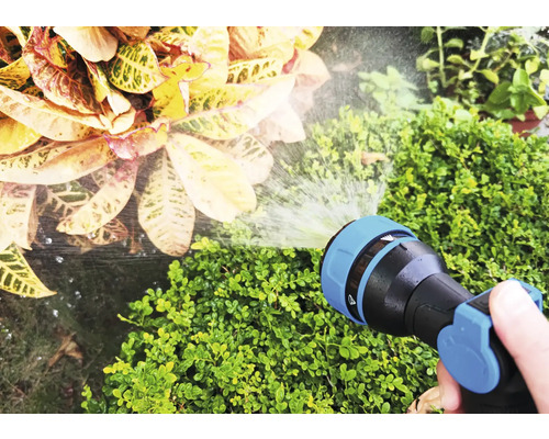 En hand håller en trädgårdsslang som vattnar växter.