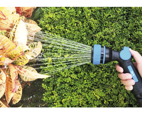 En hand håller en trädgårdsslang som vattnar växter.