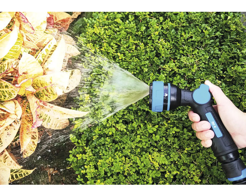 En hand håller i en trädgårdsspruta som sprutar vatten på växter.