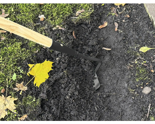 Trädgårdshacka med trähandtag som används på mörk jord