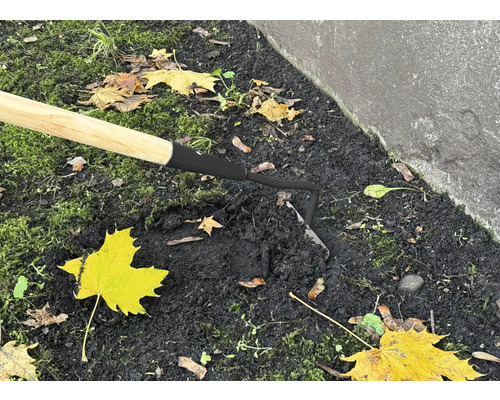 Närbild av en hacka med trähandtag i trädgårdsjorden.