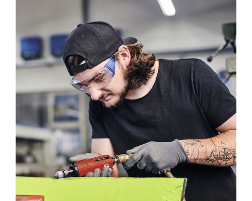 En man med skyddsglasögon och handskar använder en tryckluftsslip.