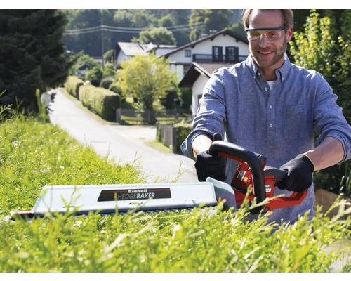 Man klipper häck med en elektrisk häcksax i trädgården.
