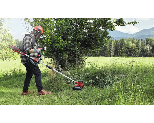 En person som använder en sladdlös grästrimmer i en gräsbevuxen utomhusmiljö.