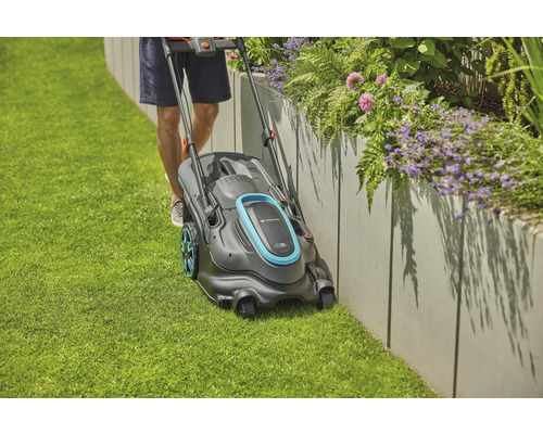 En man klipper gräsmattan med en gräsklippare längs en upphöjd blomsterrabatt