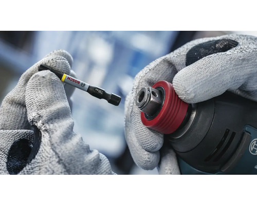 En hand med handske håller ett Bosch skruvdragarbits redo att sättas in i en sladdlös skruvdragare.