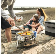 Strandscen med familj som grillar räkor och citron på en bärbar grill i rostfritt stål från Petromax