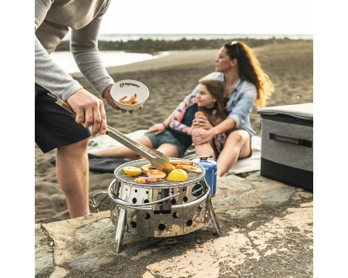 Strandscen med familj som grillar räkor och citron på en bärbar grill i rostfritt stål från Petromax