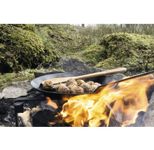 Köttbullar i en panna över en lägereld med en träslev