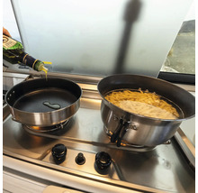 Två kastruller på en spis, i en kastrull kokar pasta, i den andra hälls olja.