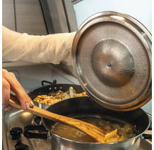 Pasta rörs om i en kastrull med en träsked medan kastrullens lock lyfts.