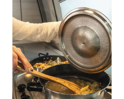 Pasta rörs om i en kastrull med en träsked medan kastrullens lock lyfts.