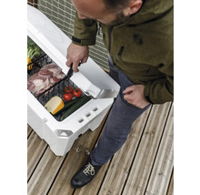 Person öppnar en vit kylbox med grönsaker och kött på en träterrass