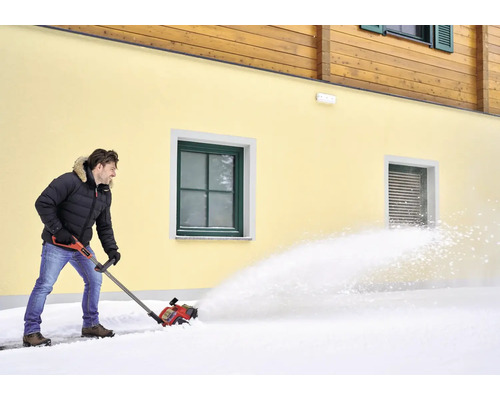 Man röjer snö med en snöslunga framför ett hus