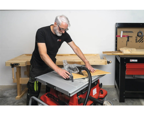 Man skär en träplatta med en bordsåg i en verkstad.